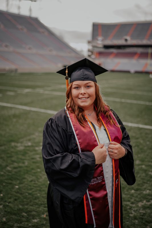 Photo of Kaylen in her cap and gown on the football field at VA Tech. 