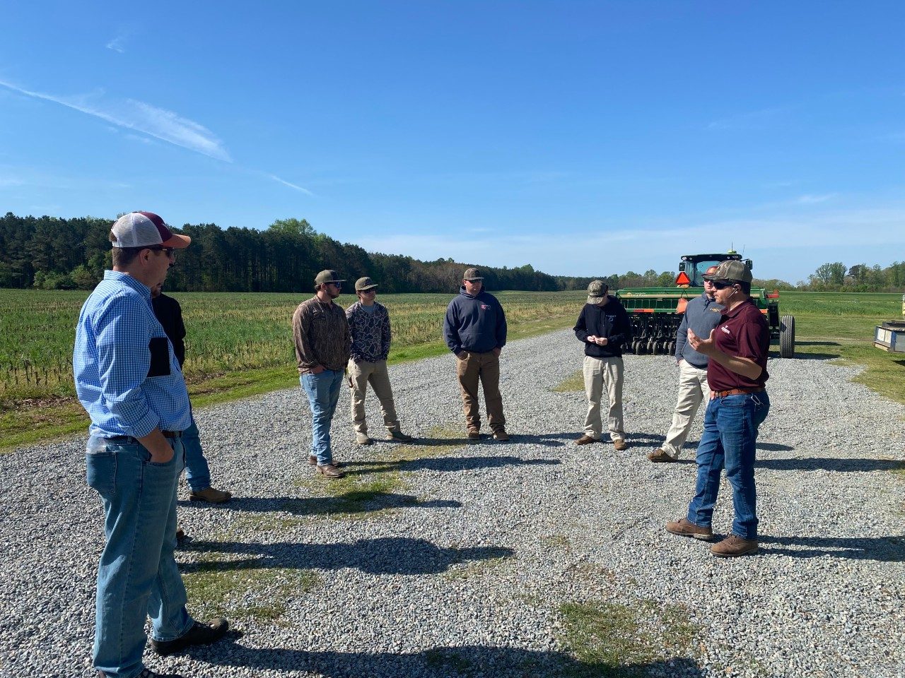students speaking with industry representatives next to a crop field and tractor